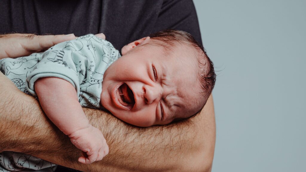 Crying baby resting on man's forearm